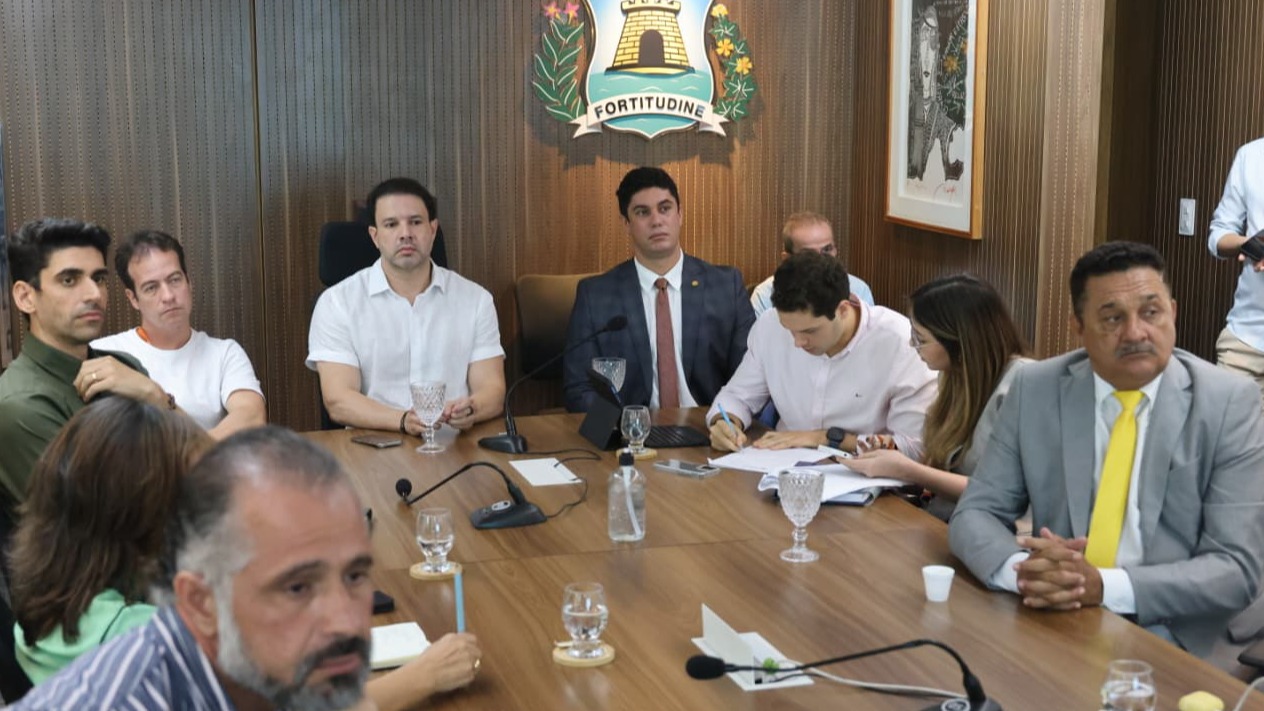 O prefeito em exercício, Leo Couto, gestores e representantes da Prefeitura e integrantes da Fifa estão sentados à mesa na sala de reuniões  do Paço Municipal